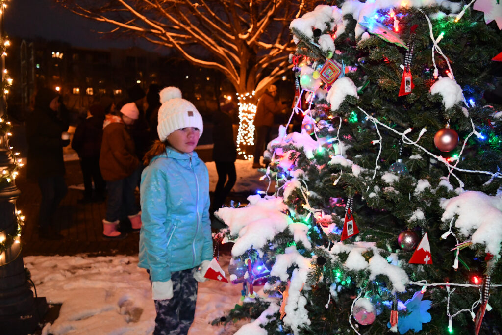 A girl standing in snow stares at a decorated tree