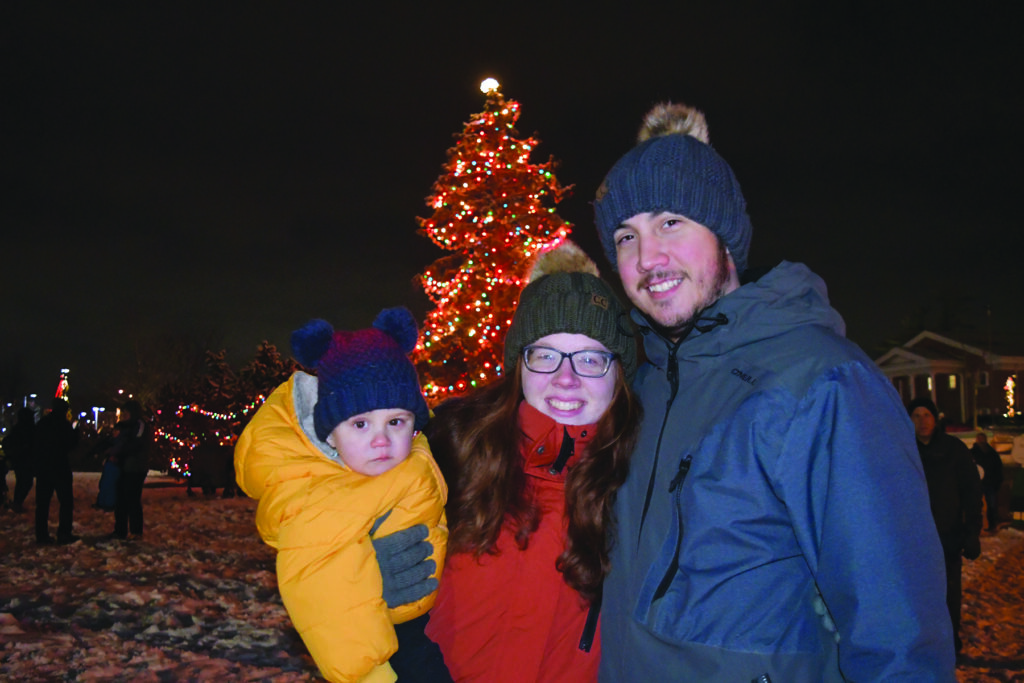 A family poses in front of the large community tree during celebration of lights