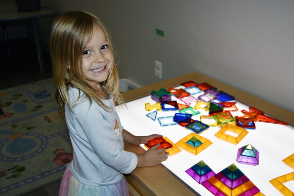A student plays with magnetic tiles at a light table.