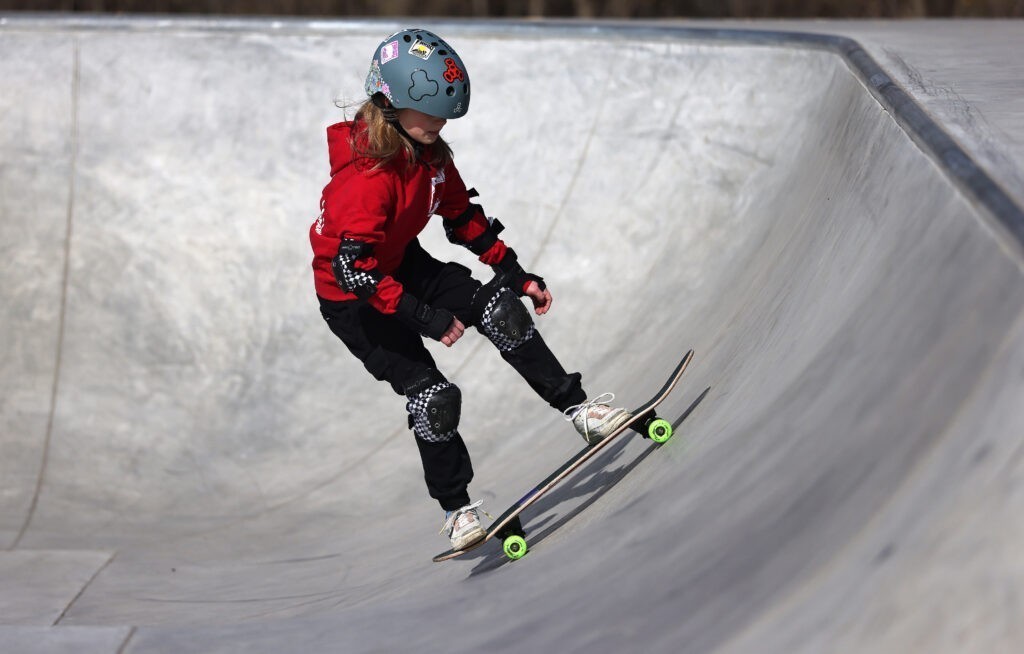 A girl age 7 wearing a helmet and protective gear skateboards up a ramp at the skate park in Clark Island Recreation Area in Batavia.