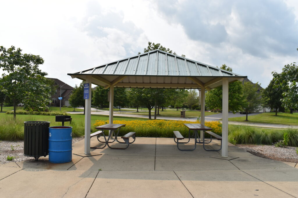 Bennett Park rentable pavilion displaying picnic tables, community grill, trash and recycling cans.