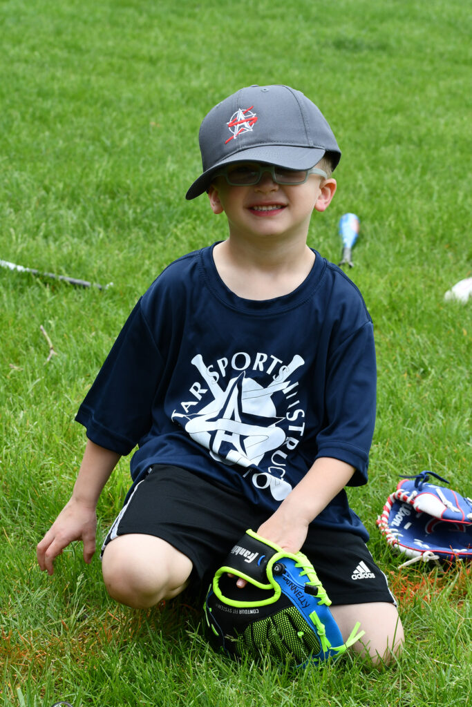 A young All Star Sports T-ball player poses with his glove and uniform shirt and hat