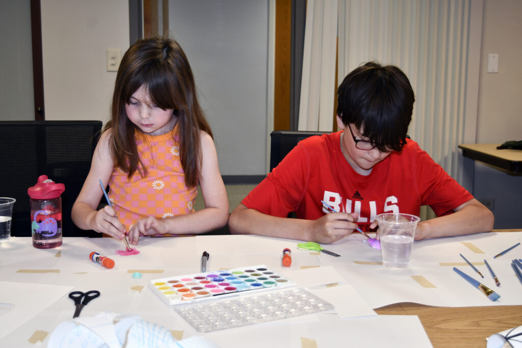 A girl and boy work on projects during summer art camp