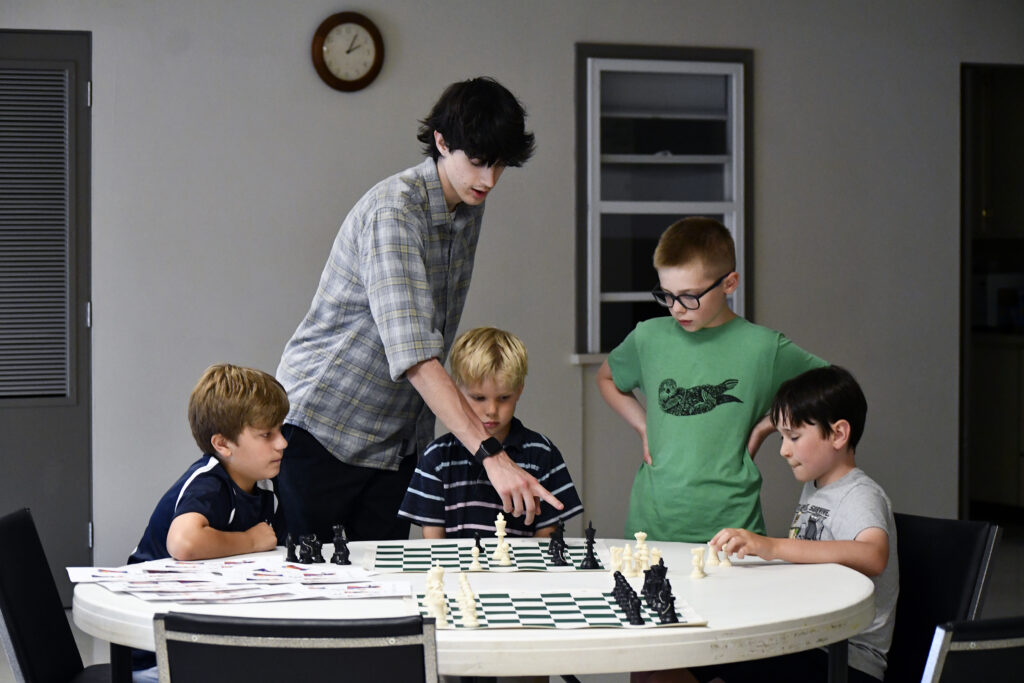 A camp counselor explains a chess move to four boys during summer chess camp