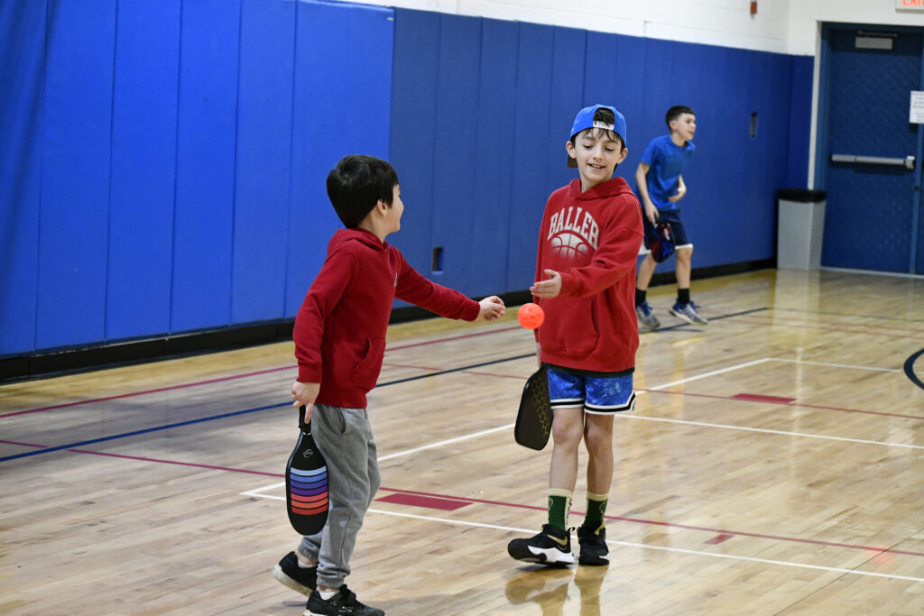 Two boys grab for the ball during pickleball summer camp