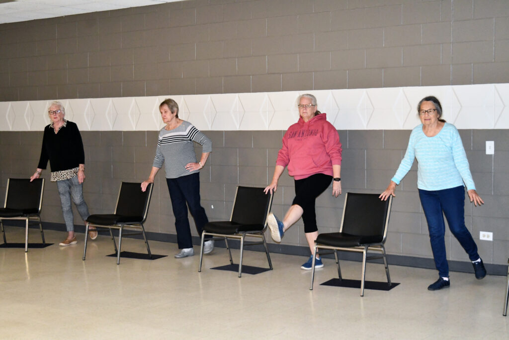 Adults balancing during a chair yoga class