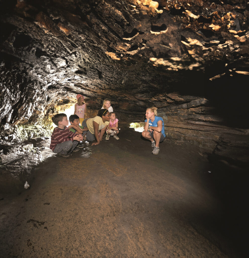 A group of kids led by an instructor takes a break inside a cave during a hike