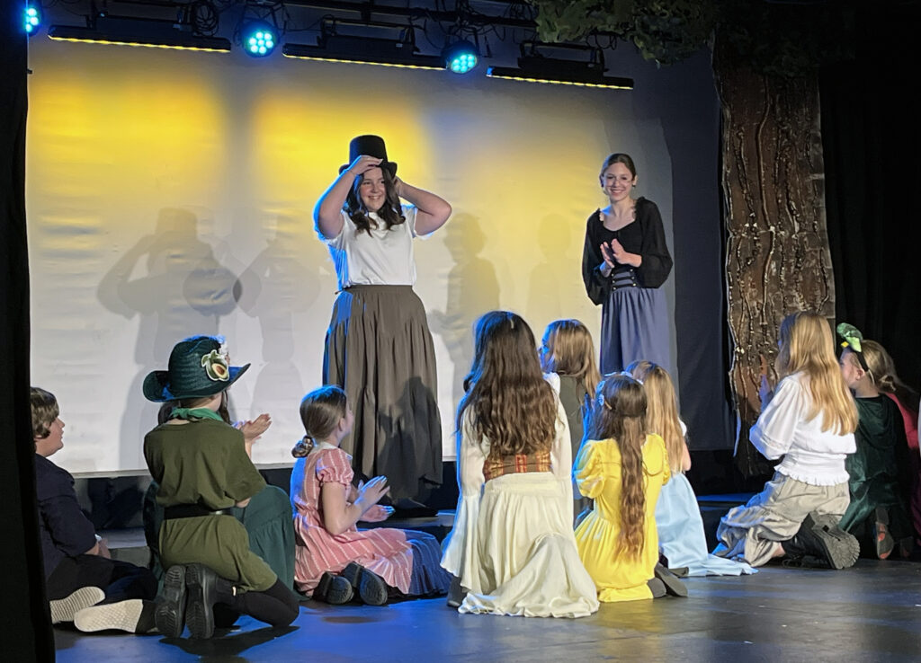 Two adult actors and a group of child actors onstage performing a play