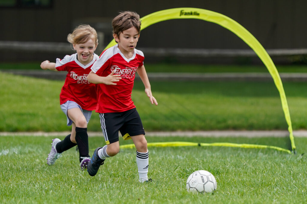 Two young soccer players run after a ball during a soccer game