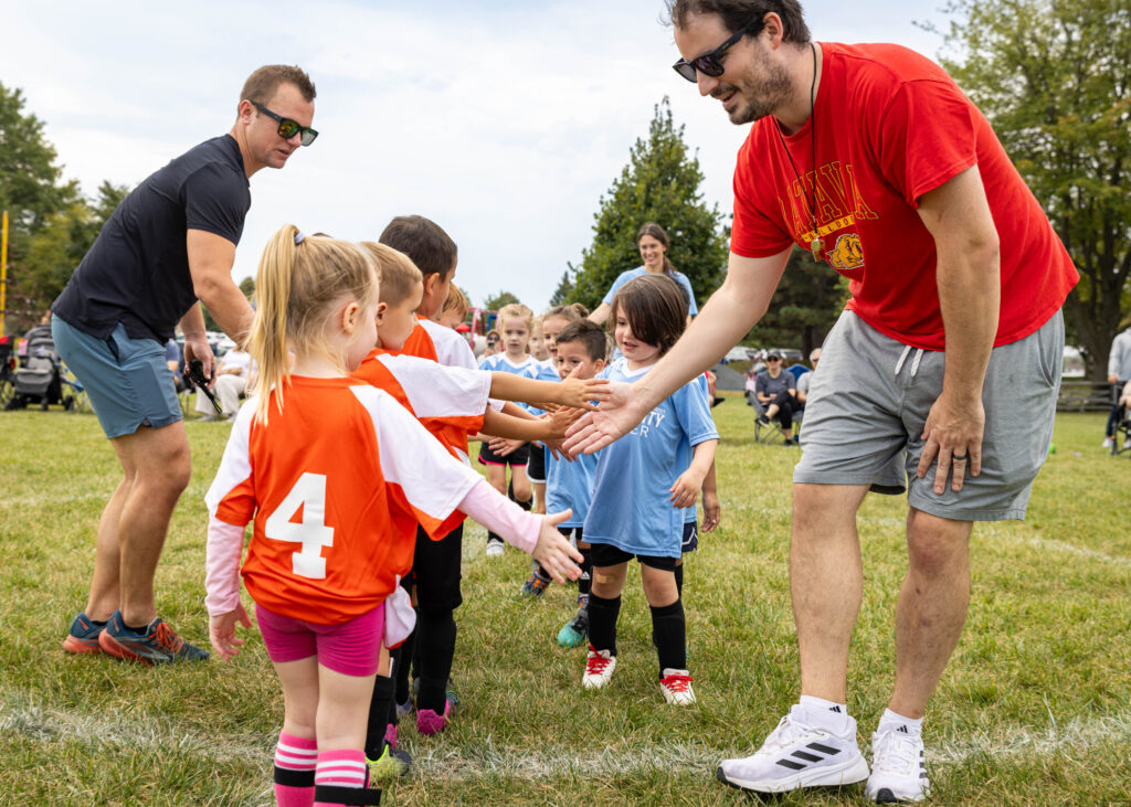 Coaches and soccer teams high five each other after playing a game