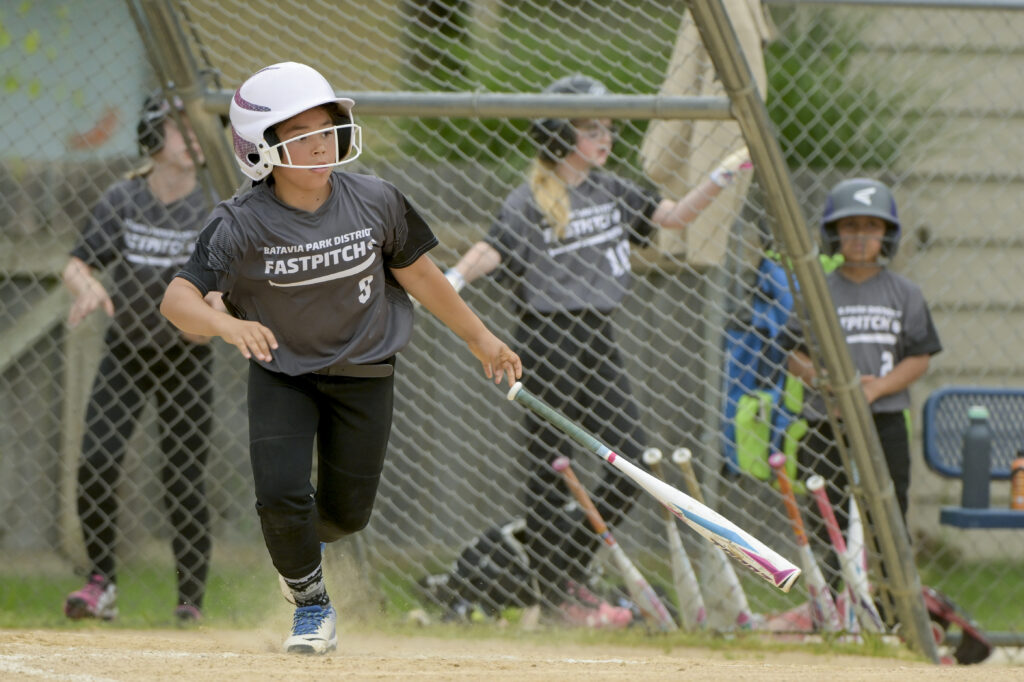 A softball player drops her bat and starts to run to first base