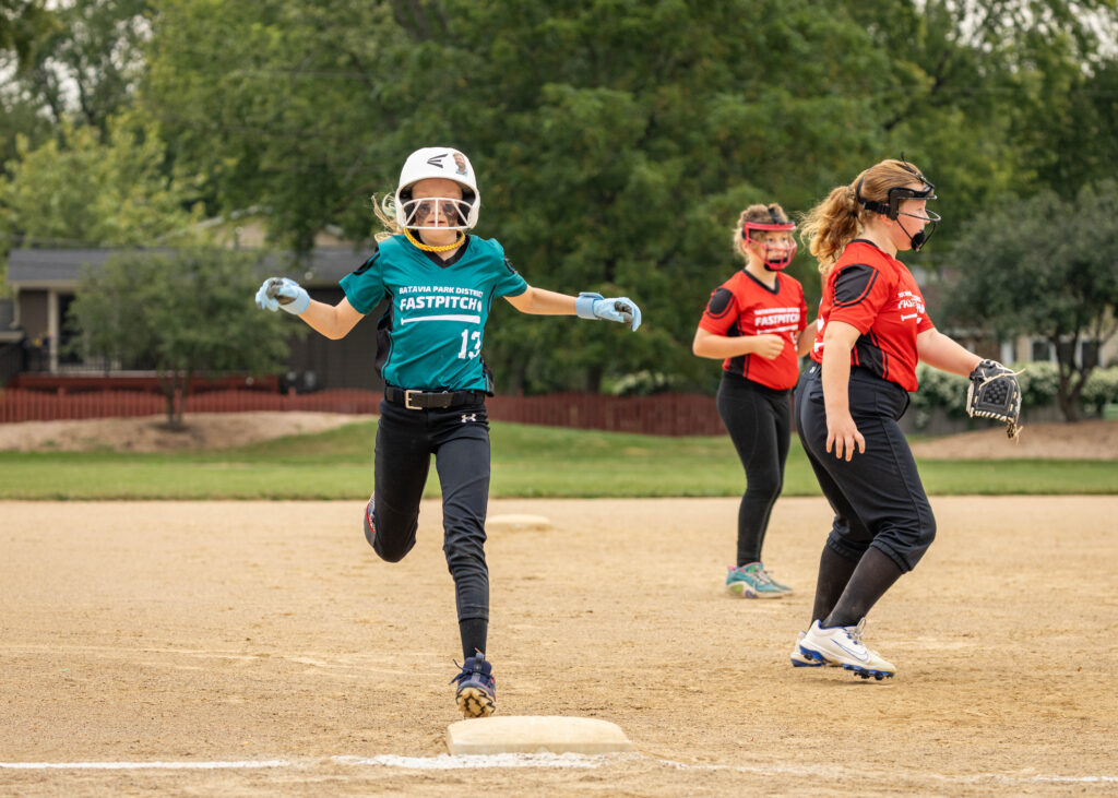 A softball player touches her foot to the base as the opposing players wait for the ball.