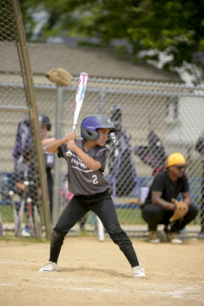 A softball player takes a batting stance with her bat at home plate as she waits for a pitch to be thrown