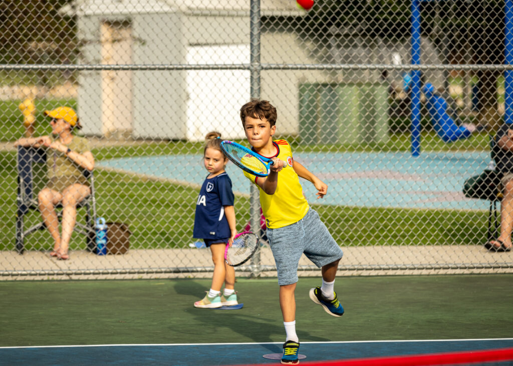 Boy aiming his racquet at the ball during outdoor tennis lessons
