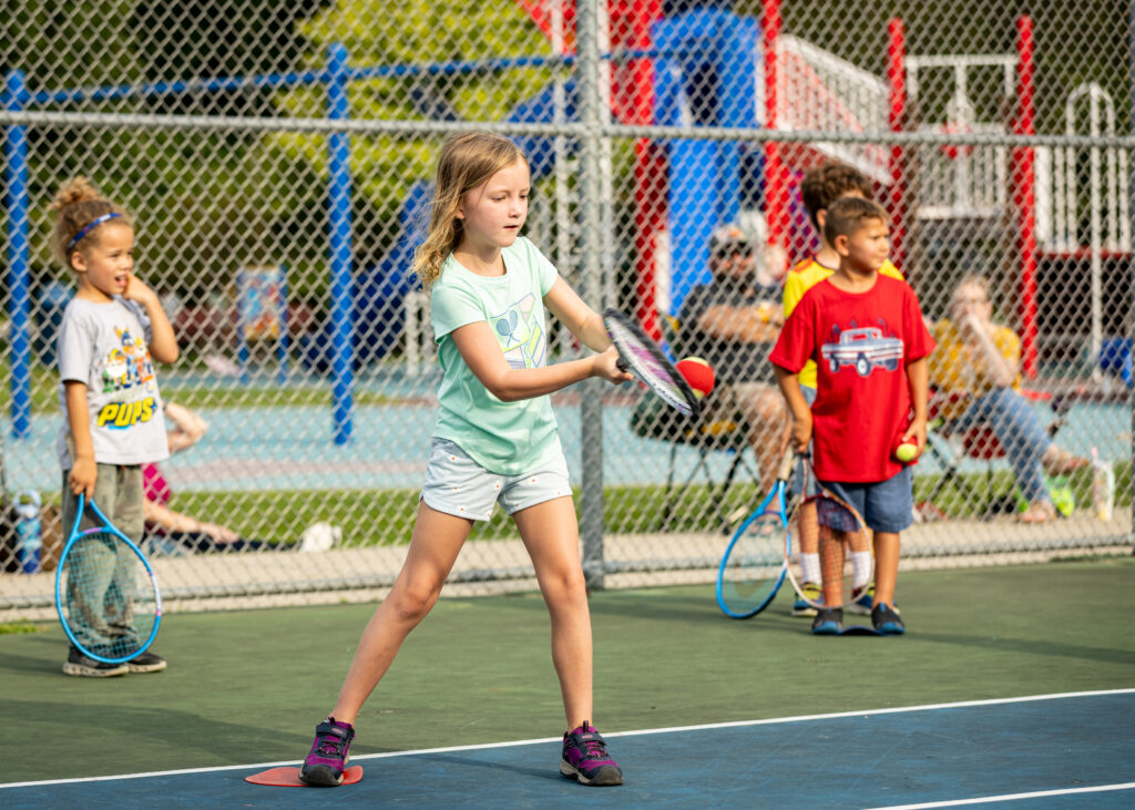 Girl taking a stance to hit the ball with her racquet during outdoor tennis lessons