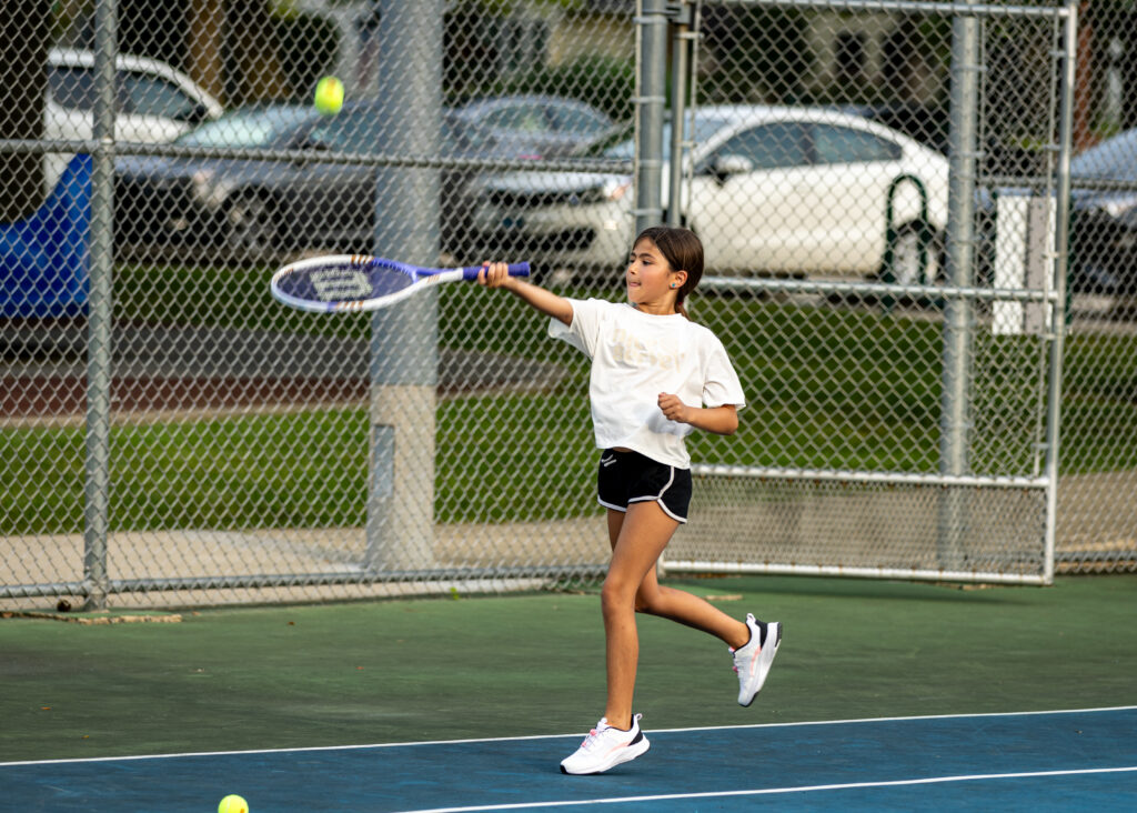 A girl positions her racquet to hit the ball during summer tennis lessons