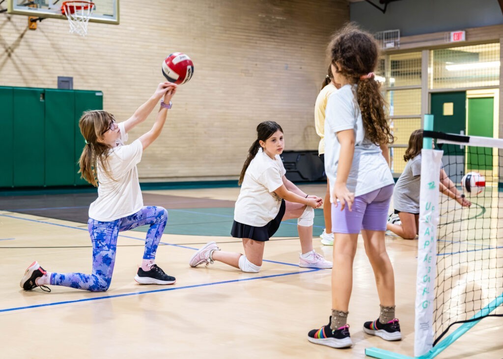 Girls volleyball class. A girl is serving as other girls watch.