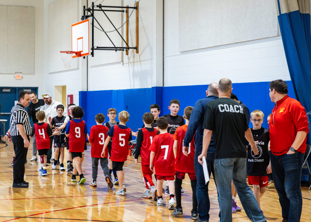 Two boys' basketball teams and their coaches line up to congratulate each team on a good game at the end of a youth basketball league game