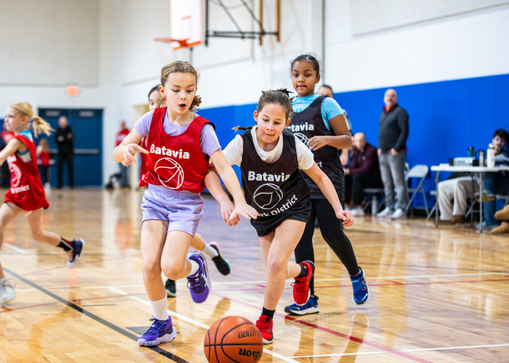 Two girls on a youth basketball league lunge for the basketball on the ground during a game