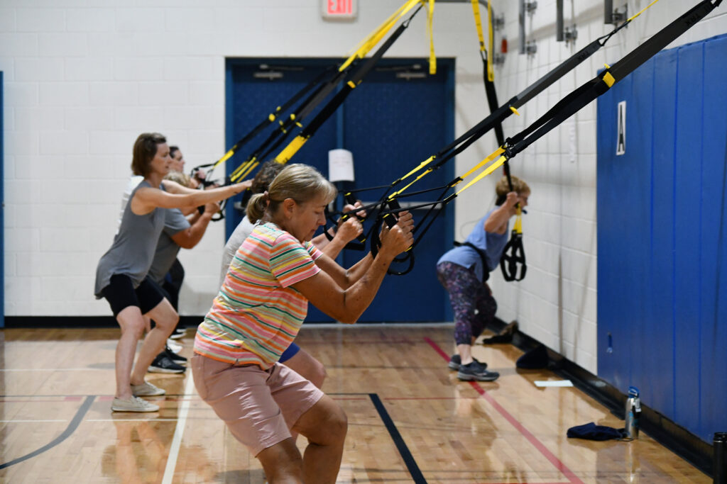 TRX class participants use the TRX straps to stretch during a TRX fitness class
