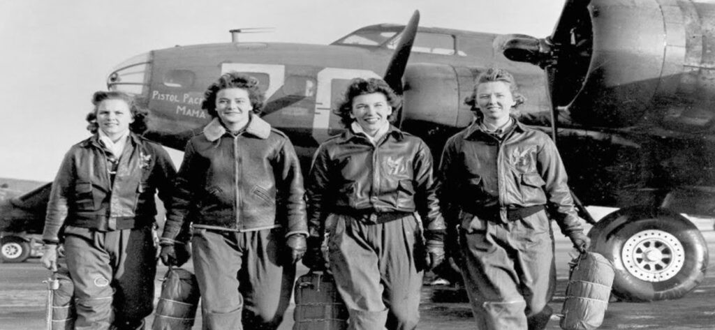 A group of women pilots walk in front of a WWII era plane