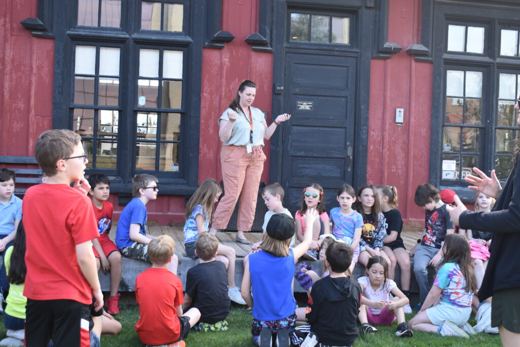 Women with school kids sitting in grass outside depot museum