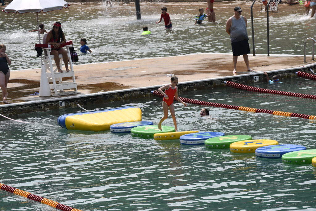 A girl hops across floating inflatable lilly pads at Hall Quarry Beach